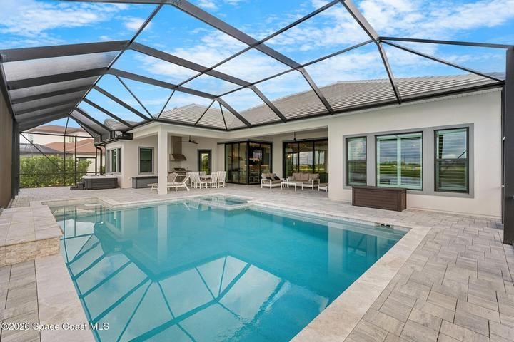 Backyard pool beneath a screened enclosure, with a modern home's patio and seating.