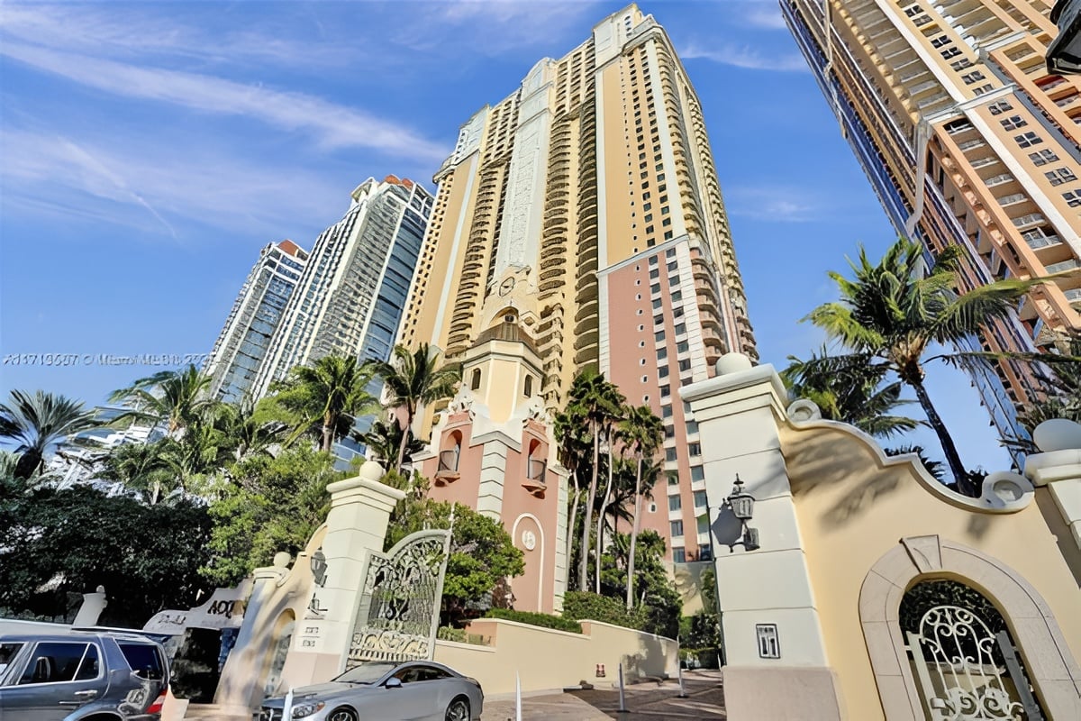 Acqualina residential towers rise behind an ornate entrance gate and palm trees.
