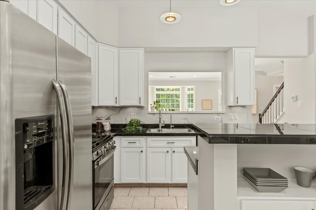 Bright kitchen with white cabinets, black countertops, a large island, and stainless steel appliances.