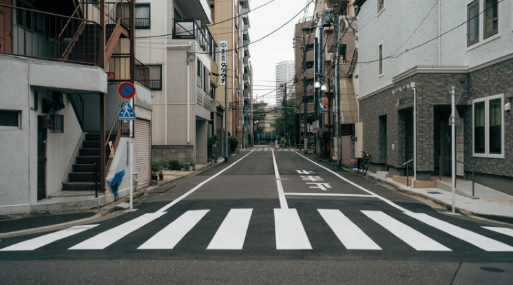 Quiet urban street with a zebra crossing, closely spaced buildings, and overhead utility wires.