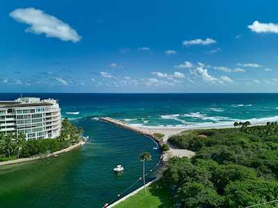 Aerial view of a coastal inlet meeting the ocean beside a beachfront condominium.