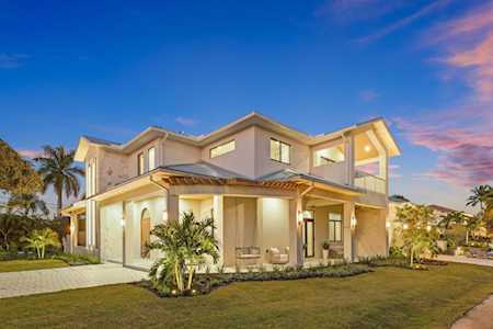 Modern two-story home with angular rooflines, glowing windows, and tropical landscaping at dusk.