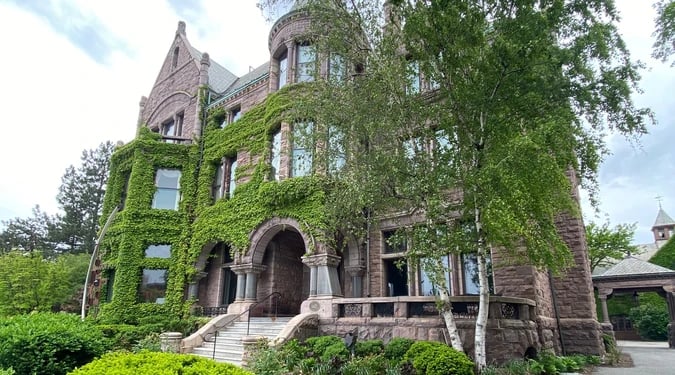 Historic stone building covered in ivy, with an arched entrance and broad front steps.