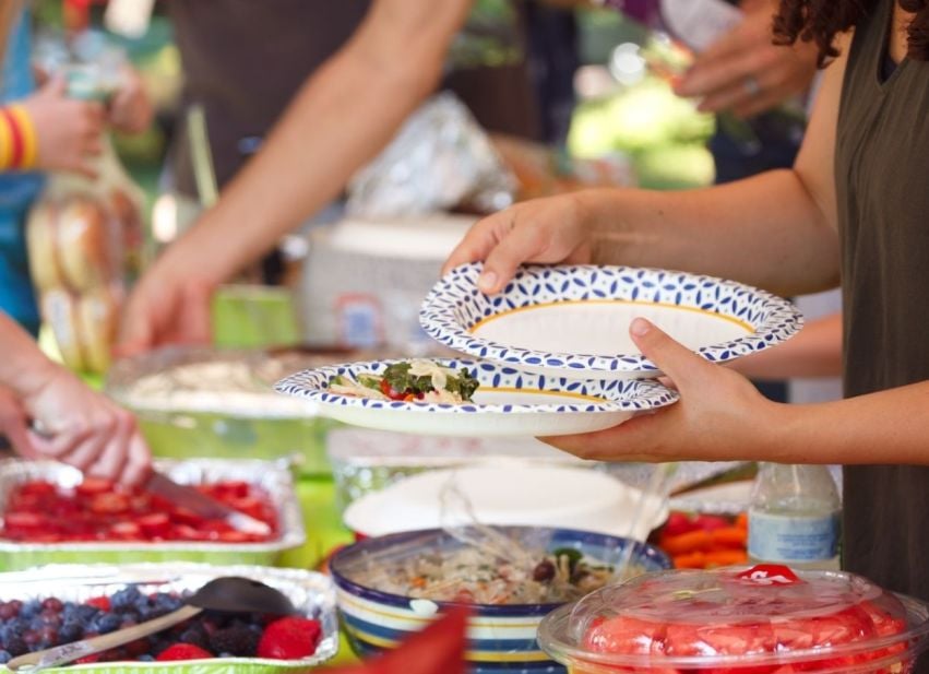 Guests serve themselves salads and fruit at an outdoor barbecue buffet.