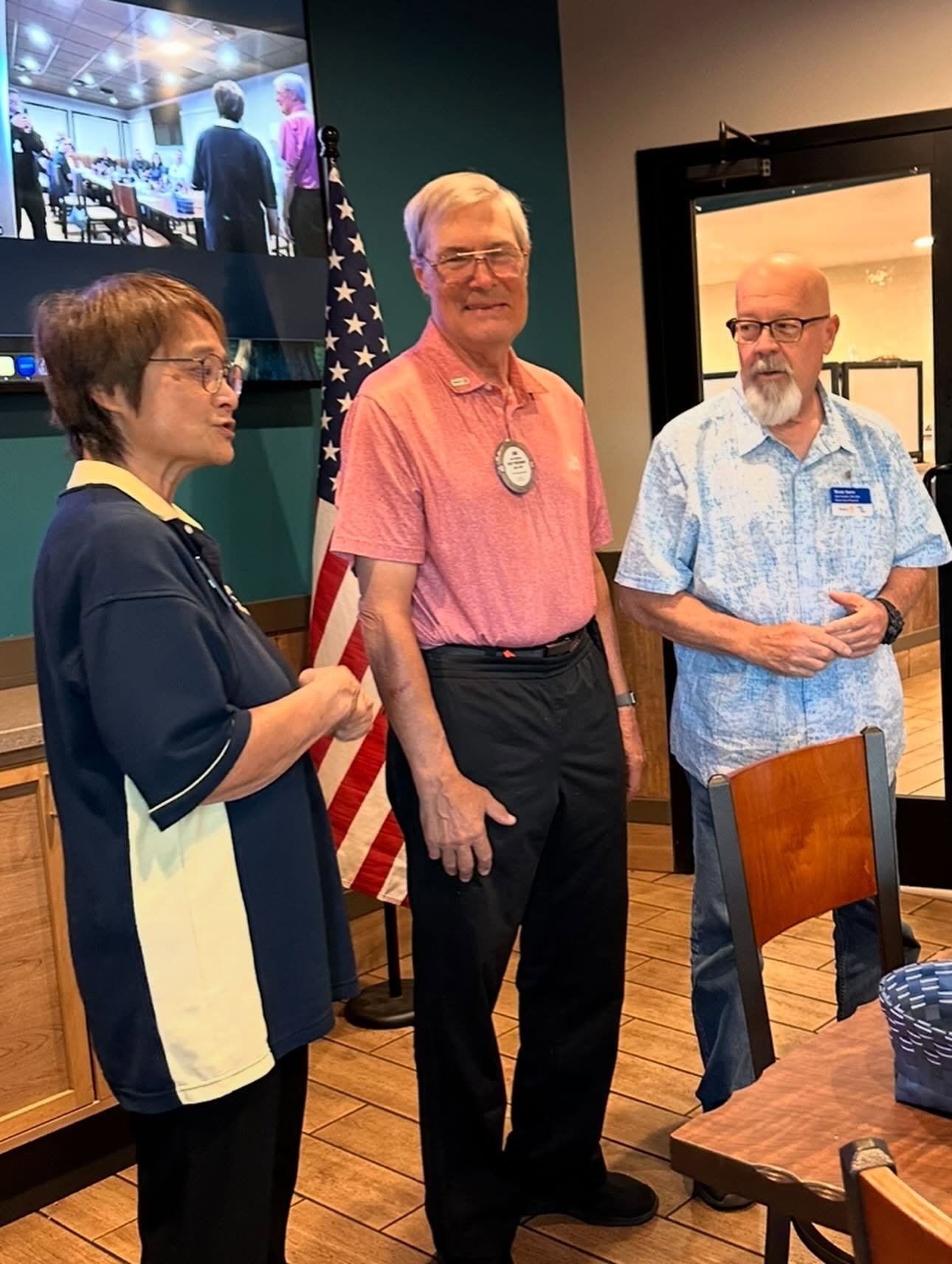 Three adults at a gathering; the man in the center wears a medal.