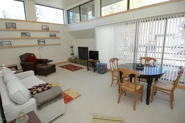 Open-plan living and dining room with vaulted windows, white seating, and a round dining table.