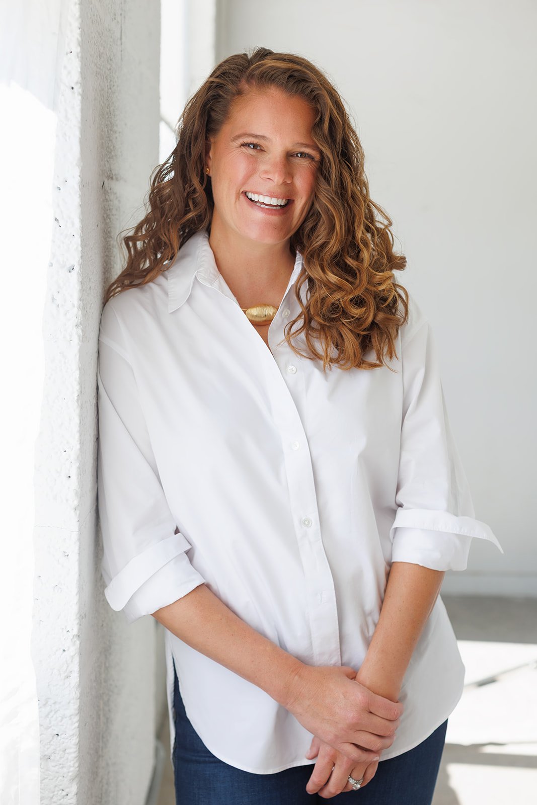 Emily Karagozian, smiling in a white shirt beside a bright window.