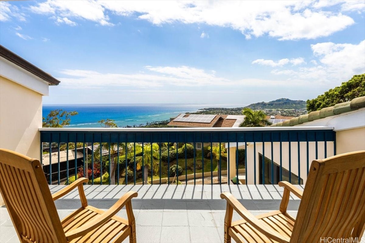 Balcony with wooden chairs overlooking the ocean and a green mountain ridge.