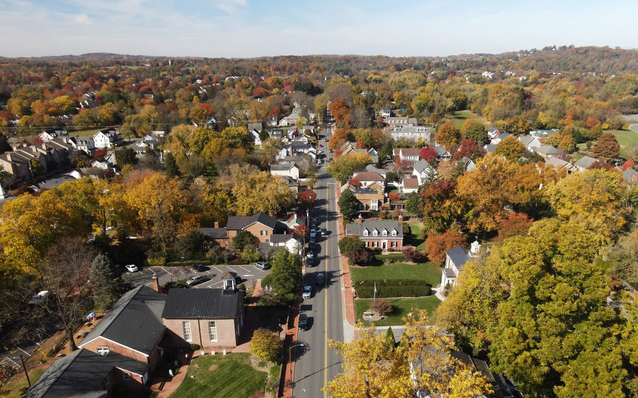 Aerial view of Waterford village, with homes along a tree-lined street and autumn-colored wooded hills beyond.