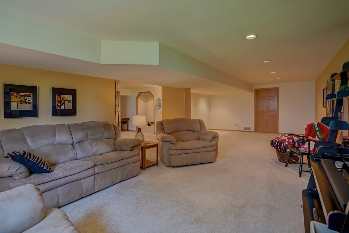 Furnished basement living room with tan sofas, beige carpet, and recessed ceiling lights.