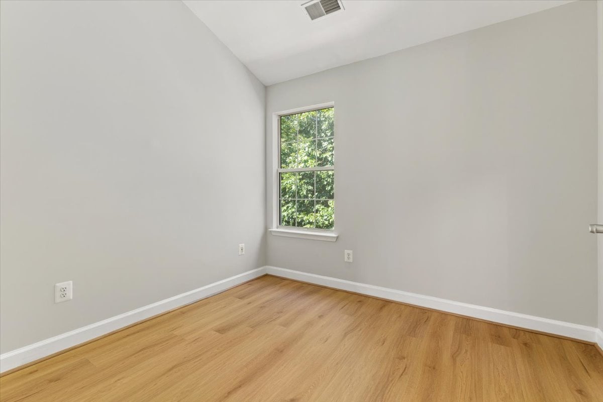 Empty room with light wood floors, a high ceiling, and a window overlooking trees.