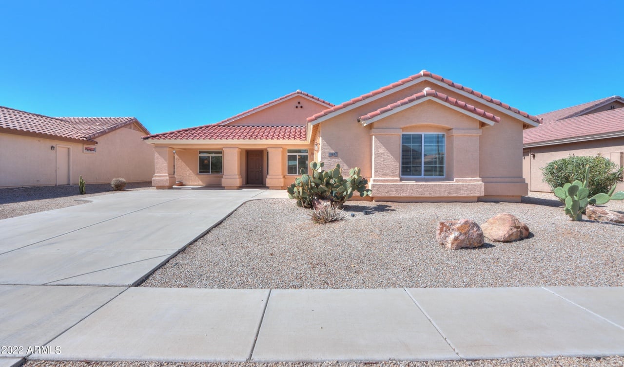 Single-story stucco home with a red tile roof, wide driveway, and gravel landscaping with cacti.