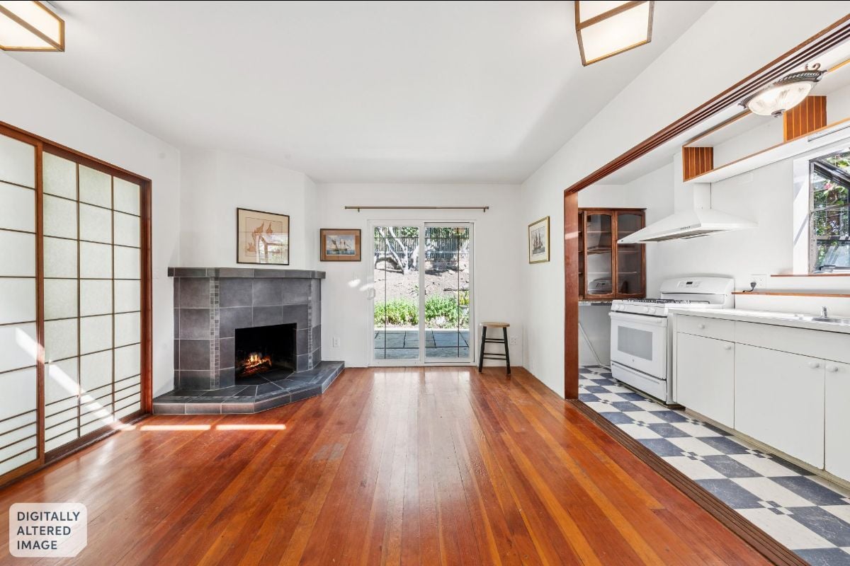 Living room with a tiled fireplace, hardwood floors, and an adjoining white kitchen.