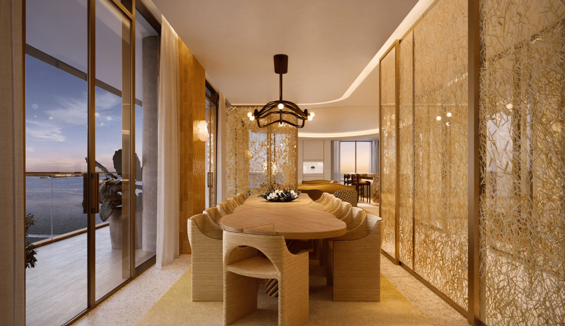 Luxury dining room with a long wooden table and water views through floor-to-ceiling windows.