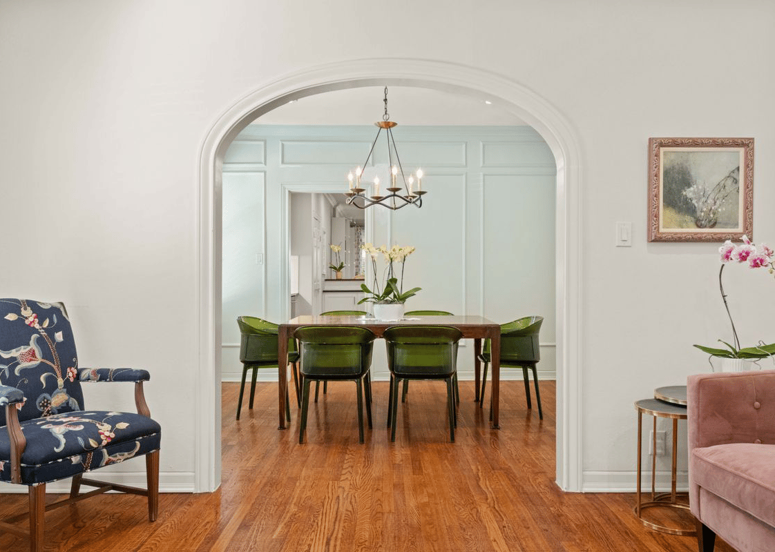 Dining room with an arched doorway, green chairs, chandelier, and hardwood floors.