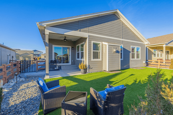 Gray home with covered patio, outdoor seating, and a bright green lawn.