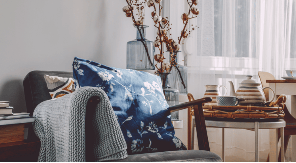Living room chair with a blue floral cushion and knitted throw beside a tea tray.