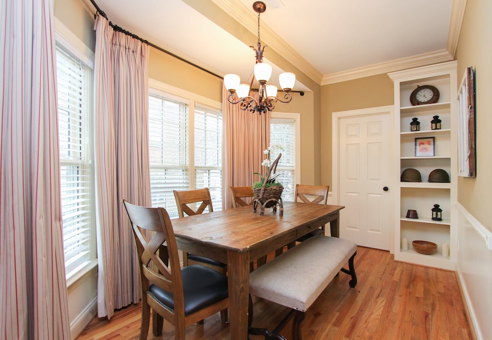 Dining room with a rustic wooden table, upholstered bench, chandelier, and built-in shelves.