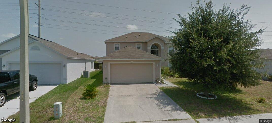 Two-story beige house with an attached garage, arched upper window, and large leafy tree beside the driveway.