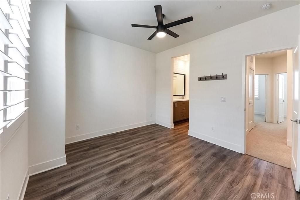  A bright empty bedroom with wood-like flooring, a modern black ceiling fan, and an en-suite bathroom visible through the doorway.