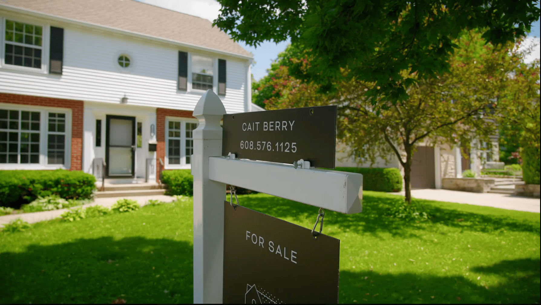 A Cait Berry of Insiders Realty For Sale sign staked in the front yard of a two-story white and brick Madison, Wisconsin home on a sunny day, representing a thoughtfully prepared home ready for the market.