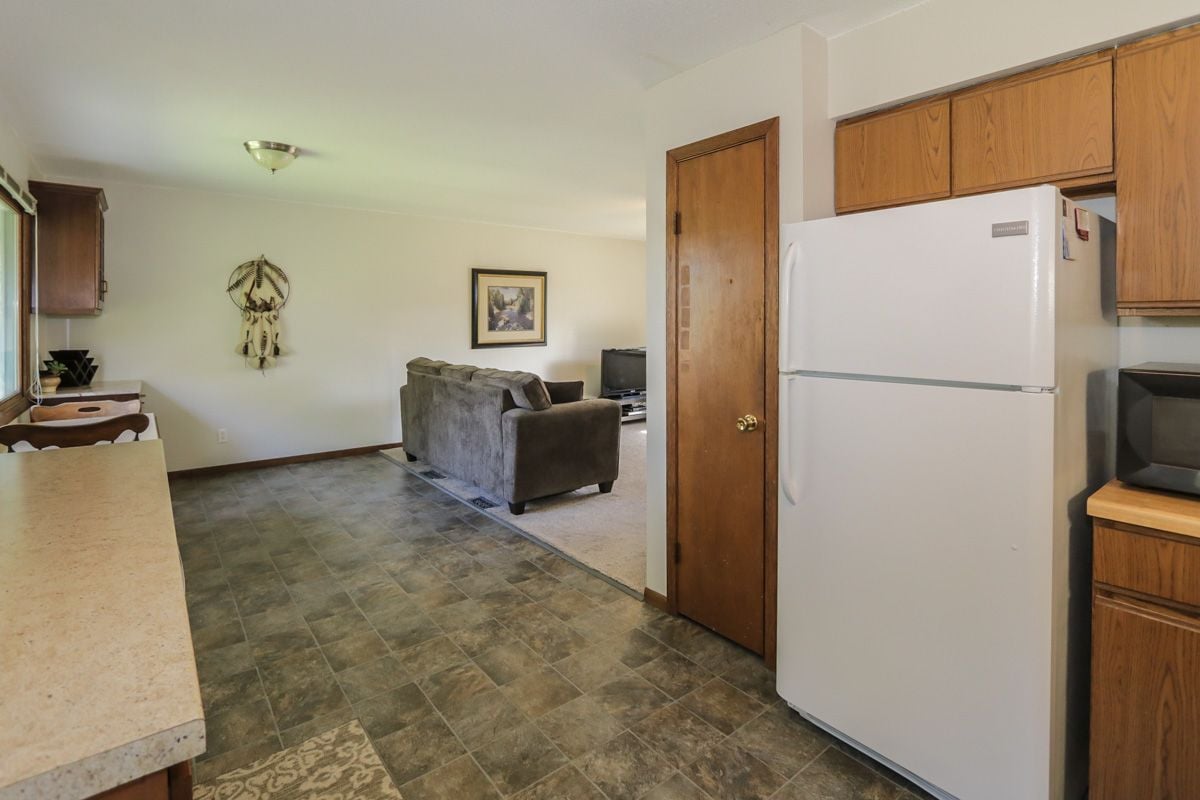 Kitchen with wood cabinets and white refrigerator opening into a living room with a gray sofa.