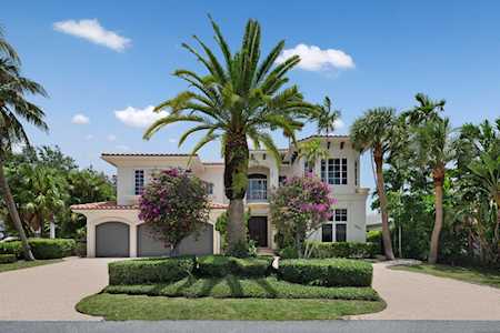 Two-story stucco home with a circular driveway, landscaped island, and surrounding palm trees.
