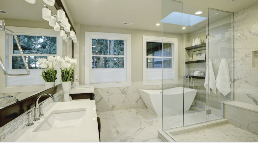 Marble bathroom with a double-sink vanity, freestanding tub, and glass-enclosed shower.