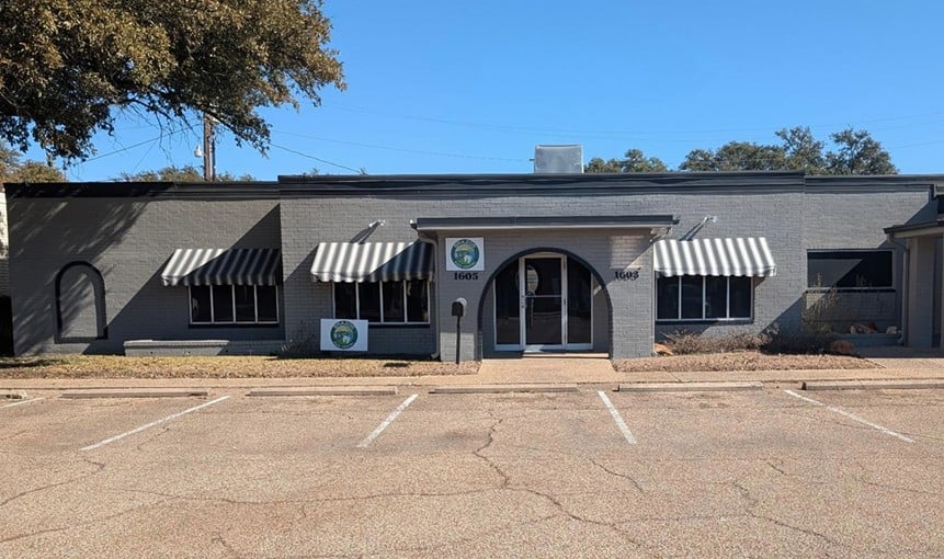 Gray commercial building with striped awnings, an arched entrance, and front parking spaces.