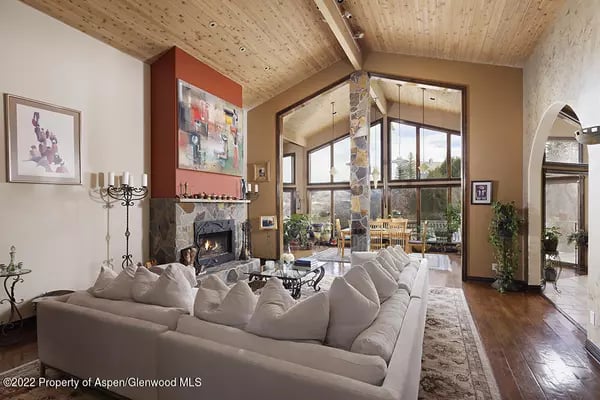 Living room with a white sectional, stone fireplace, vaulted wood ceiling, and tall windows.