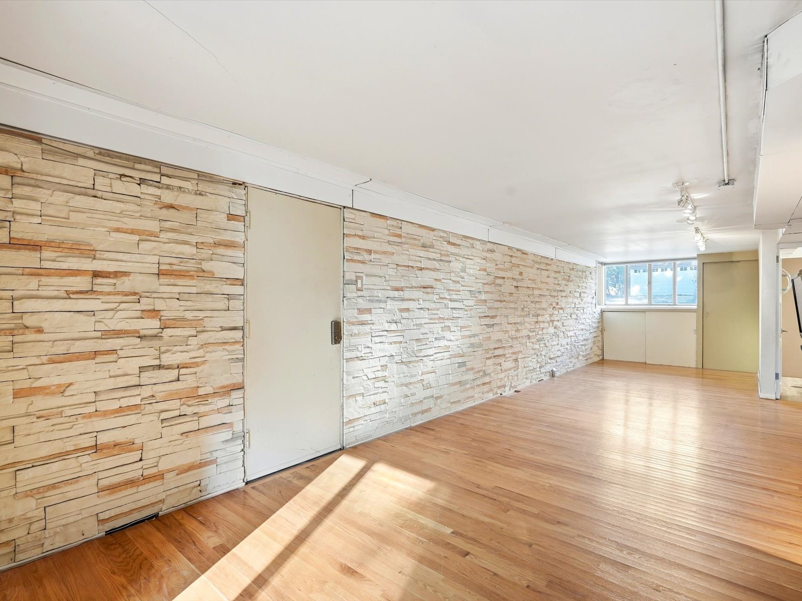 Vacant interior room with hardwood floors, stacked-stone walls, and windows at the far end.