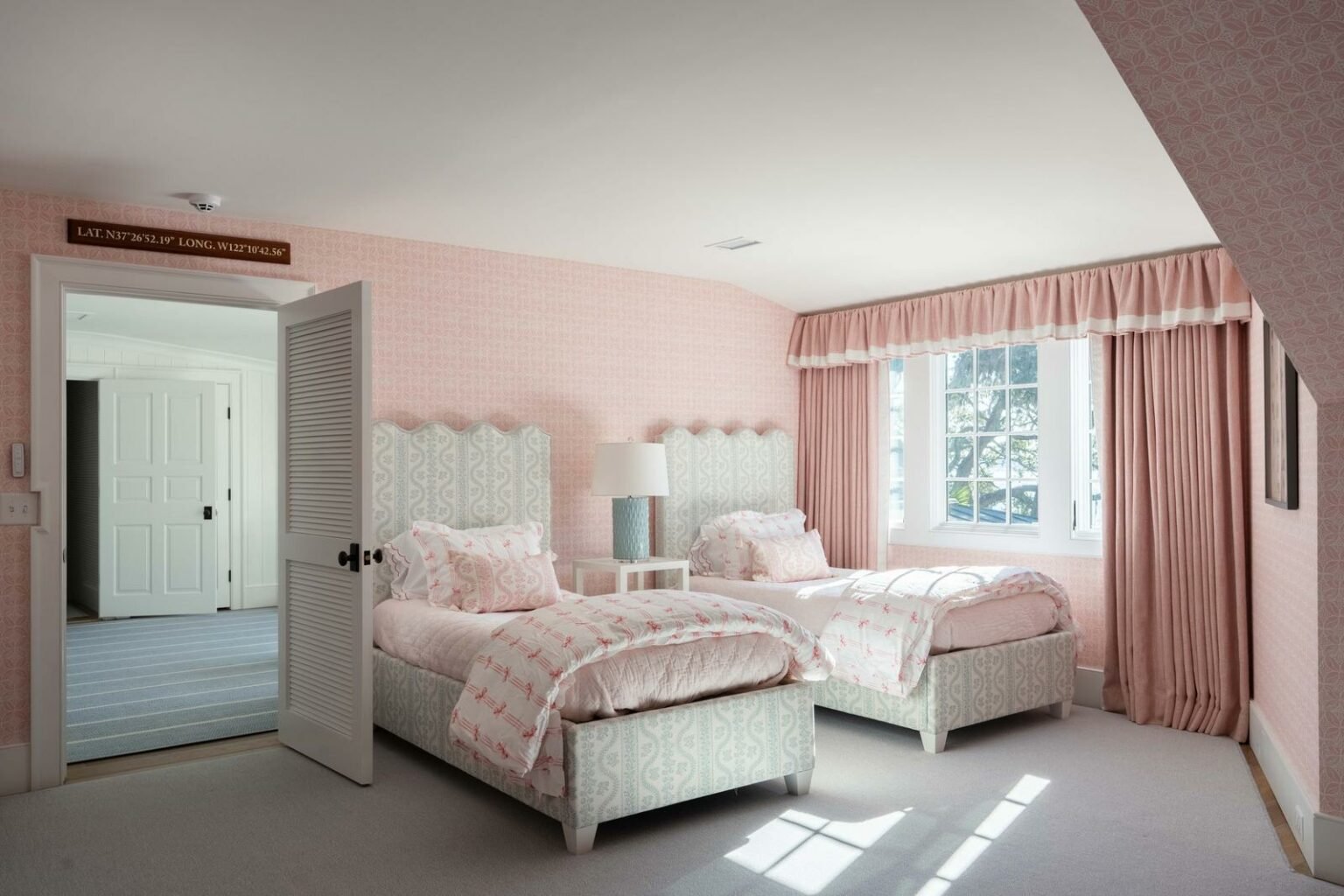 Twin bedroom with pink patterned decor, matching curtains, and sunlight streaming through the window.