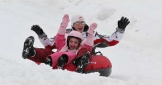 A group rides a red snow tube down a snowy slope with their arms raised.