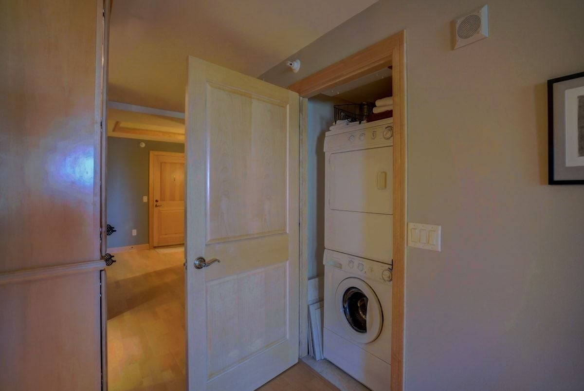 Laundry closet with stacked washer and dryer behind an open paneled door.