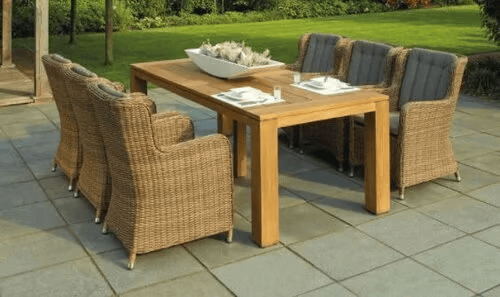 Paved patio with a wooden dining table, wicker chairs, and a green lawn beyond.
