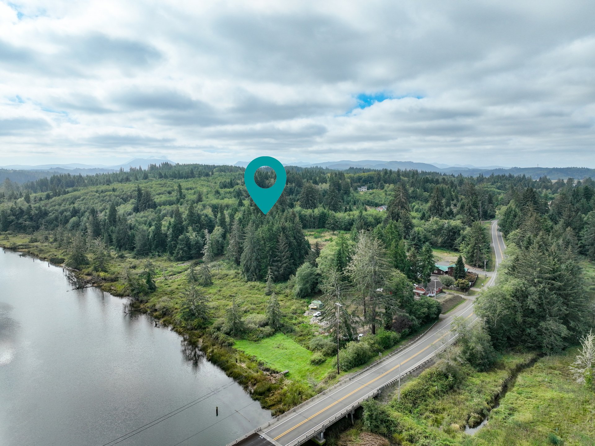 Aerial view of wooded land beside a waterway, marked with a teal pin near a road and bridge.