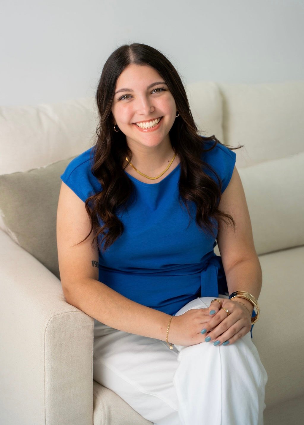 Smiling woman in a blue top seated on a light armchair.