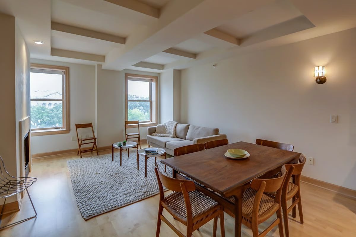 Living and dining room with a coffered ceiling, wooden furniture, and two large windows.