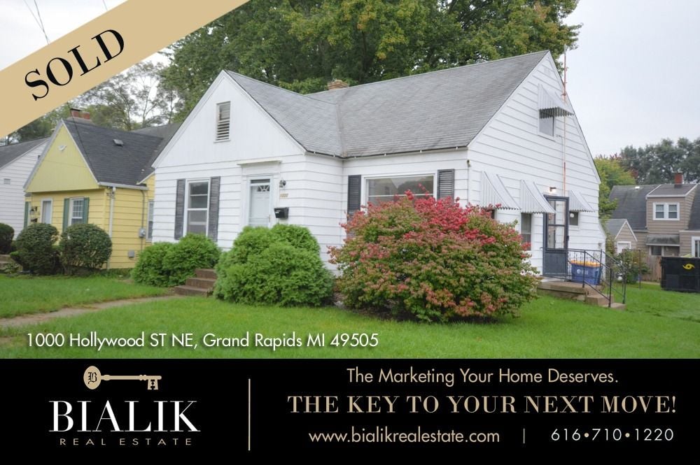 White-sided Grand Rapids home with a SOLD banner and pink-flowering shrubs in front.