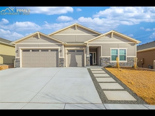 Beige single-story home with stone accents, two-car garage, and a broad concrete driveway.