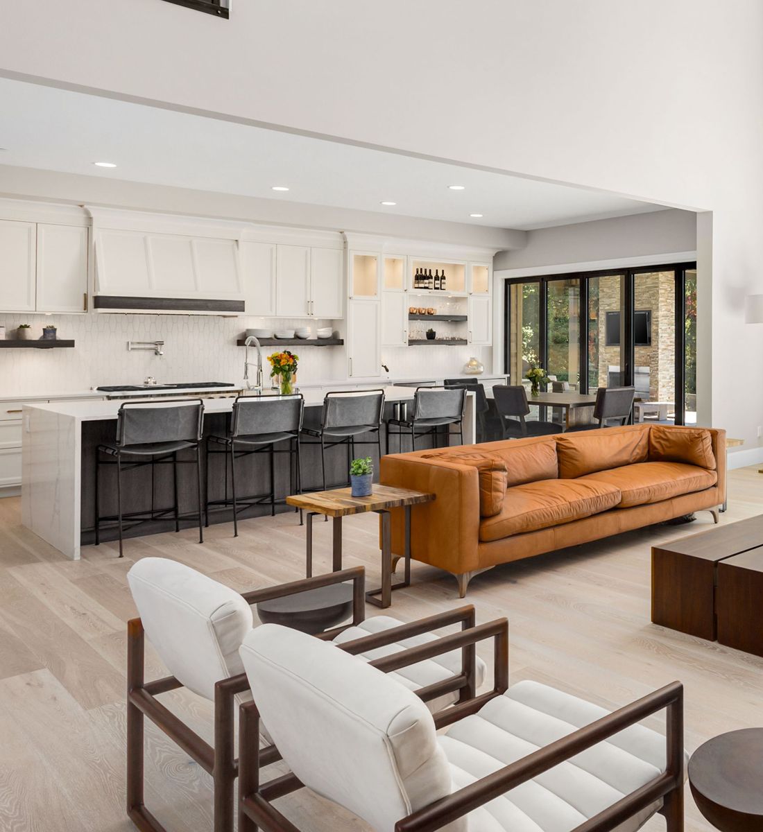 Open-plan kitchen and living area with a white island, orange leather sofa, and sliding patio doors.