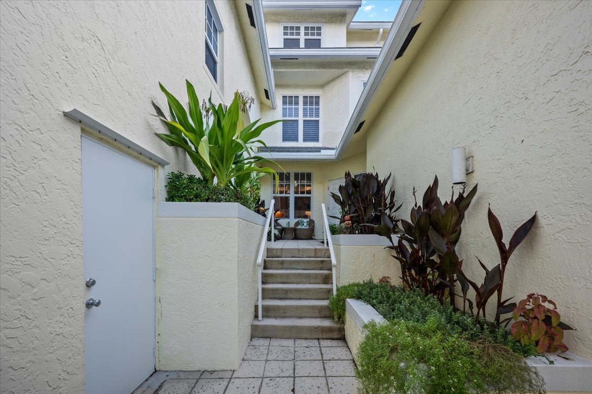 Condominium courtyard entry with central stairs, tiled walkway, and tropical landscaping.