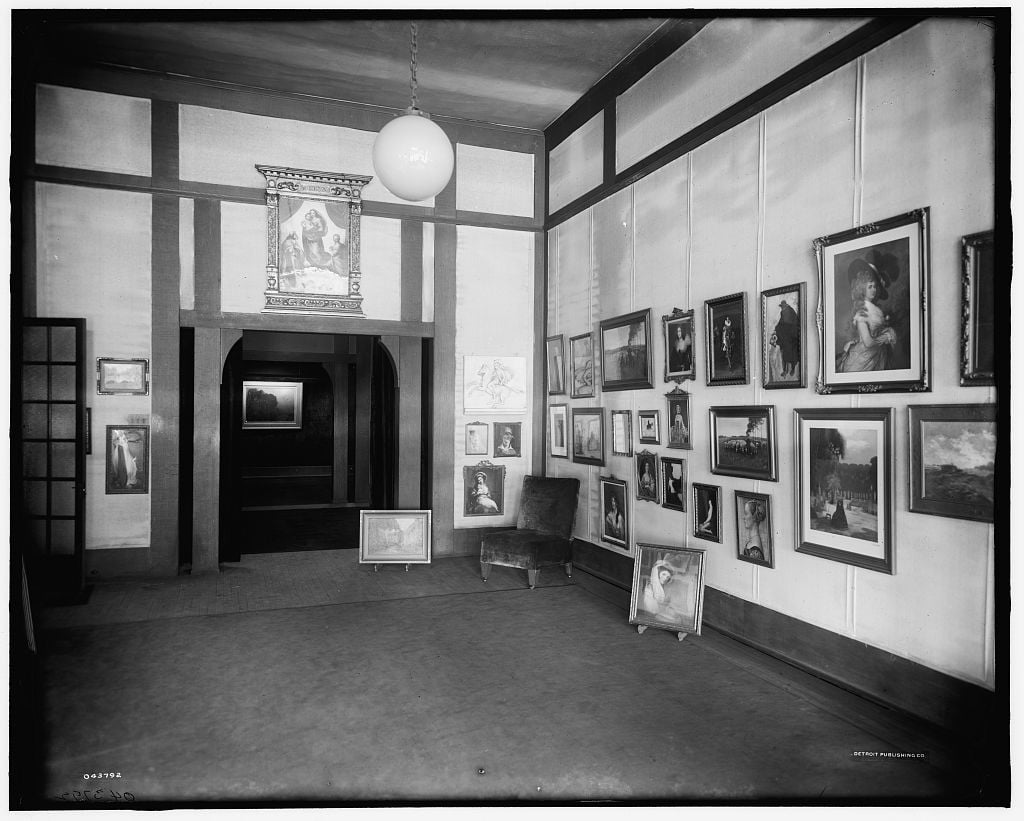 Historic art gallery interior with paintings covering the walls and a globe light.