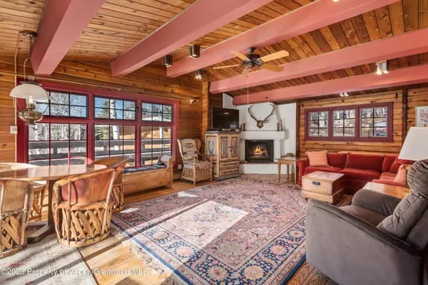 Rustic living room with exposed timber beams, large windows, and a stone fireplace.