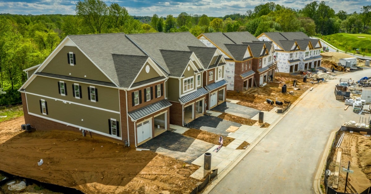 An aerial view of a housing development street with a row of townhomes ranging from finished to unfinished.