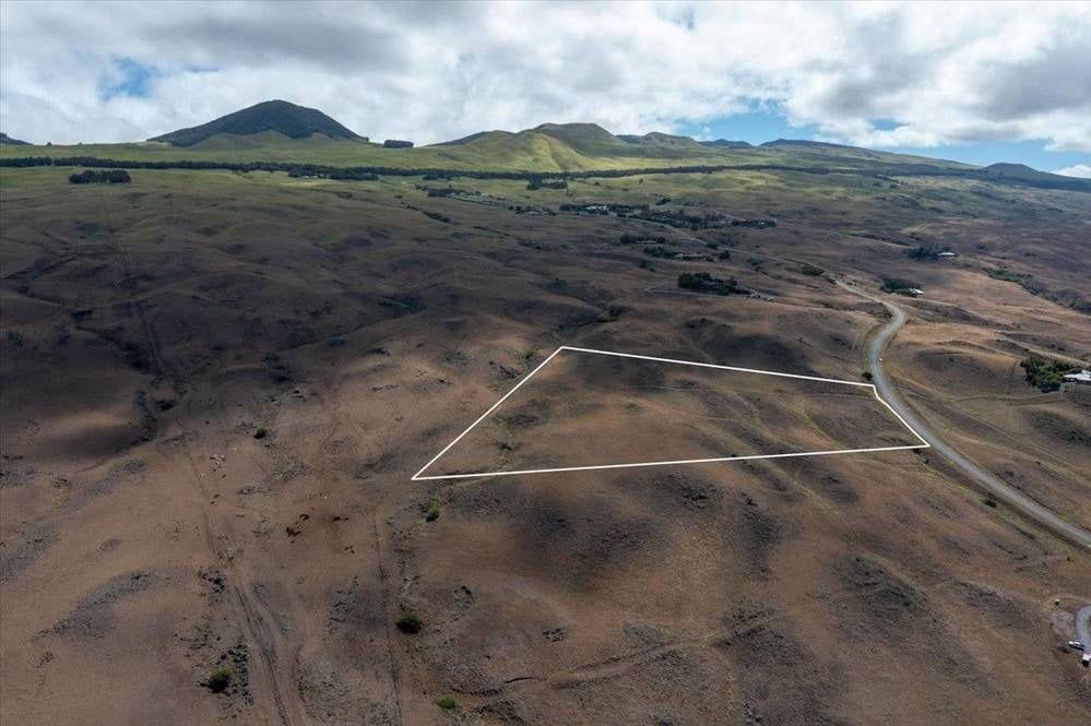 Aerial view of a vacant lot outlined beside a winding road, with rolling hills beyond.
