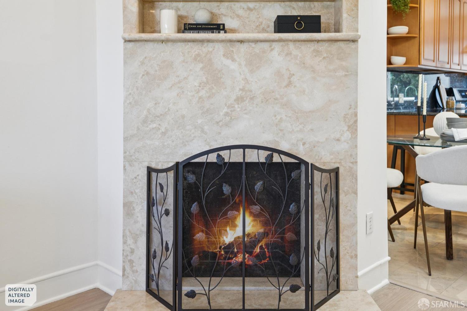 Marble-surround fireplace with a lit fire and ornate black screen in a furnished interior.