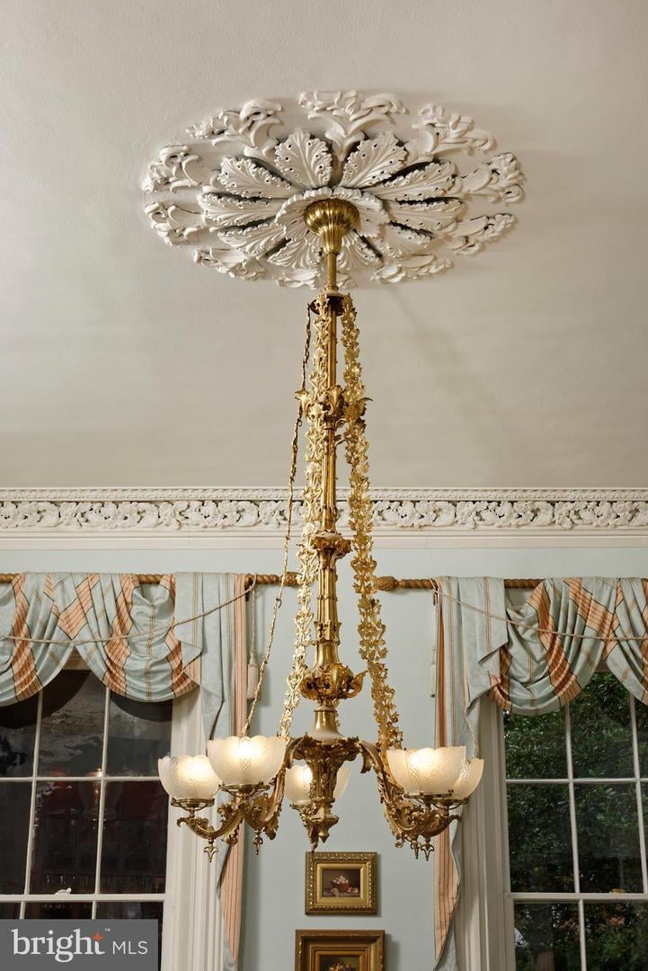 Ornate gold chandelier beneath a carved ceiling medallion, with draped windows in the background.