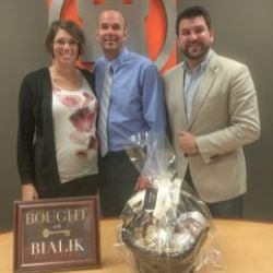 Three adults celebrate a closing beside a “Bought Bialik” sign and gift basket.