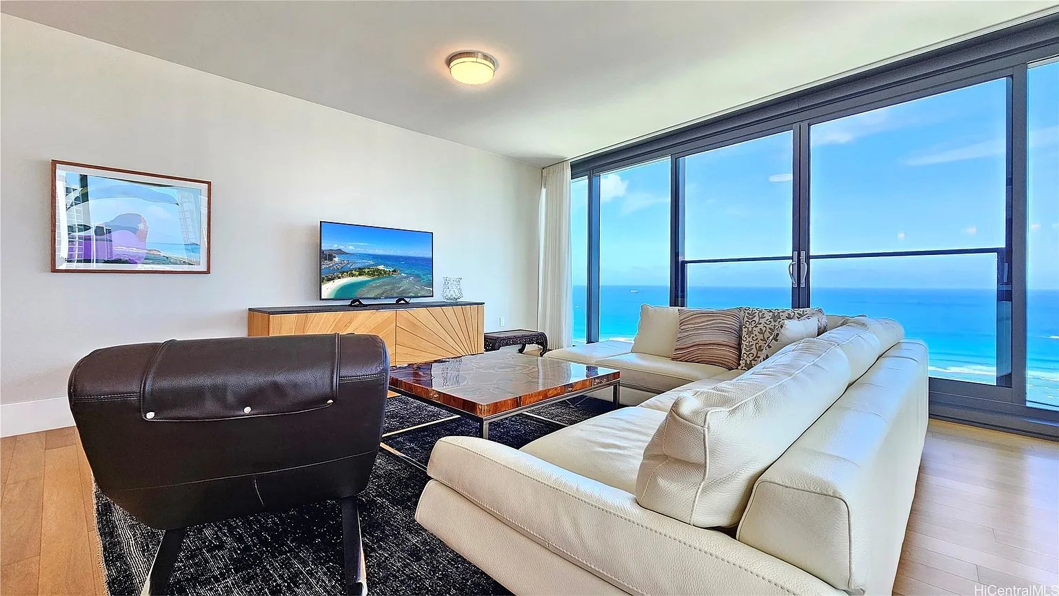 Living room with a white sectional and floor-to-ceiling windows overlooking the ocean.